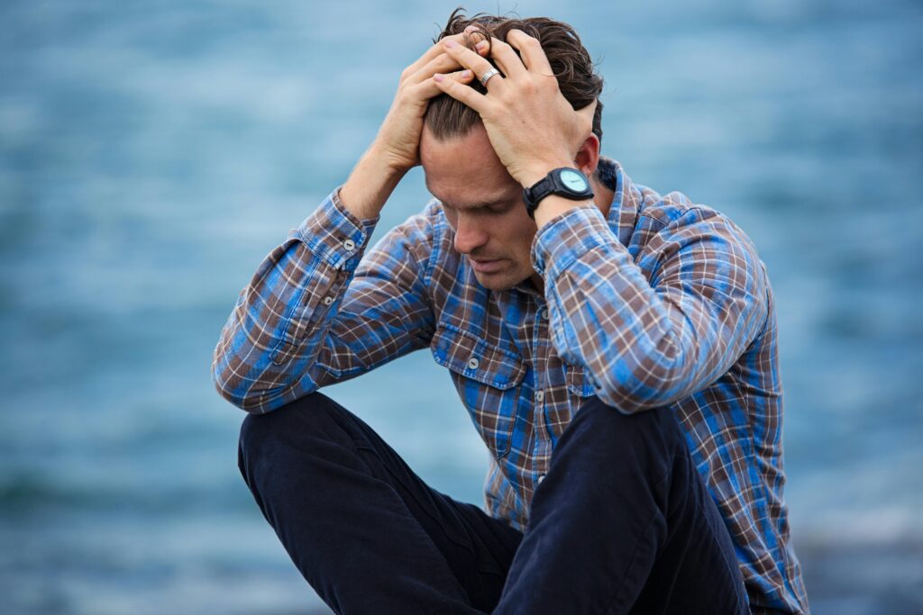 pexels-photo-897817-897817 A man in a plaid shirt sits by the water looking distressed, symbolizing stress.